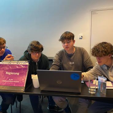 Schüler sitzen um einen Leptop und schauen gemeinsam auf den Bildschirm